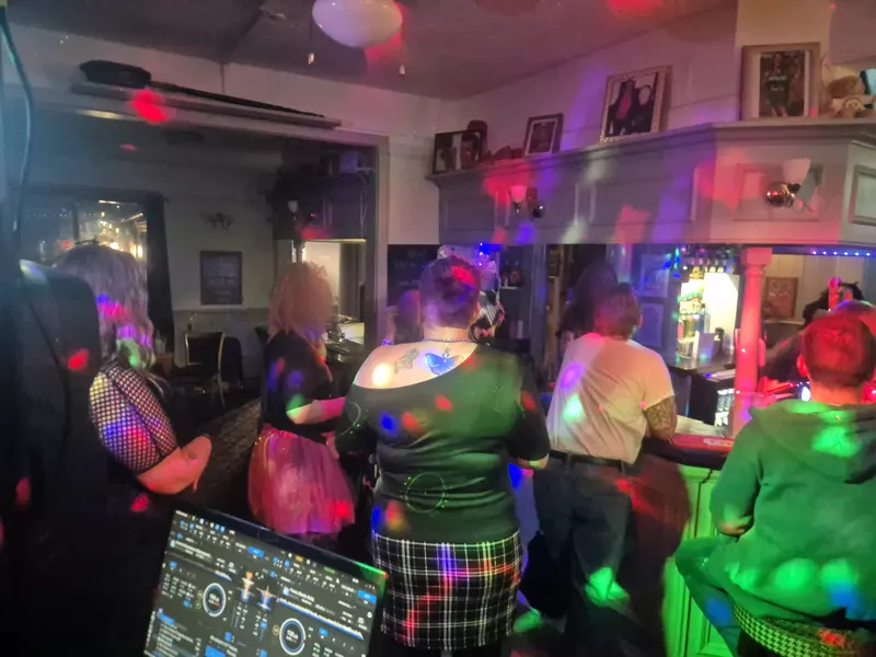 The dance floor seen from behind the DJ laptop, guests in neon and tartan