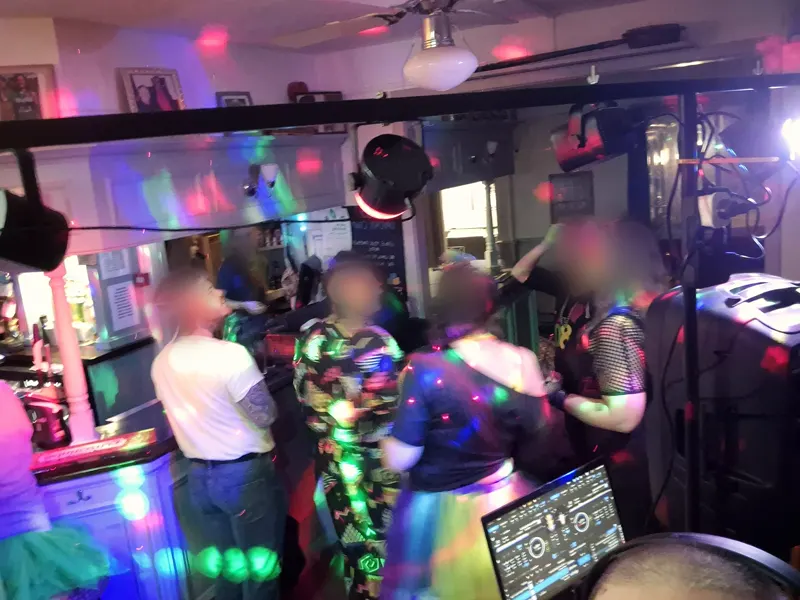 Guests in 80s fancy dress dancing in front of the DJ decks under party lights