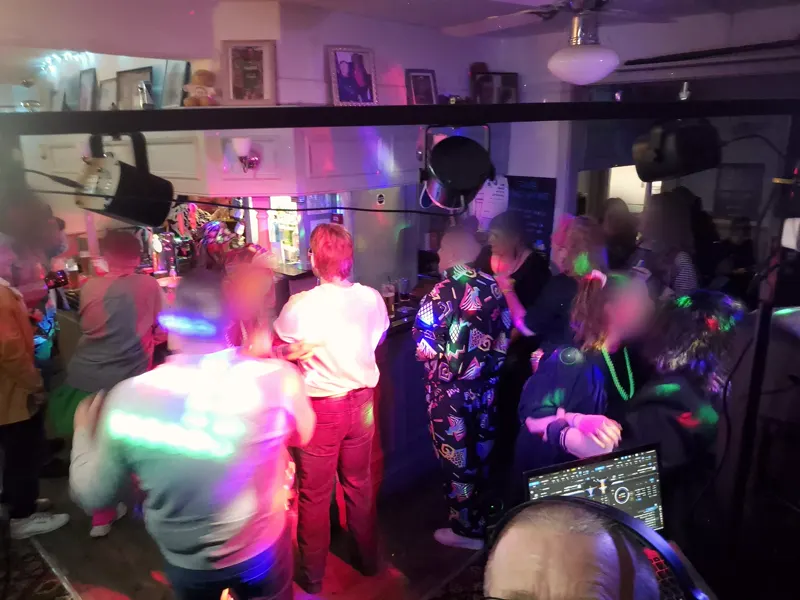 Packed pub dance floor with coloured party lights and the DJ controller in view