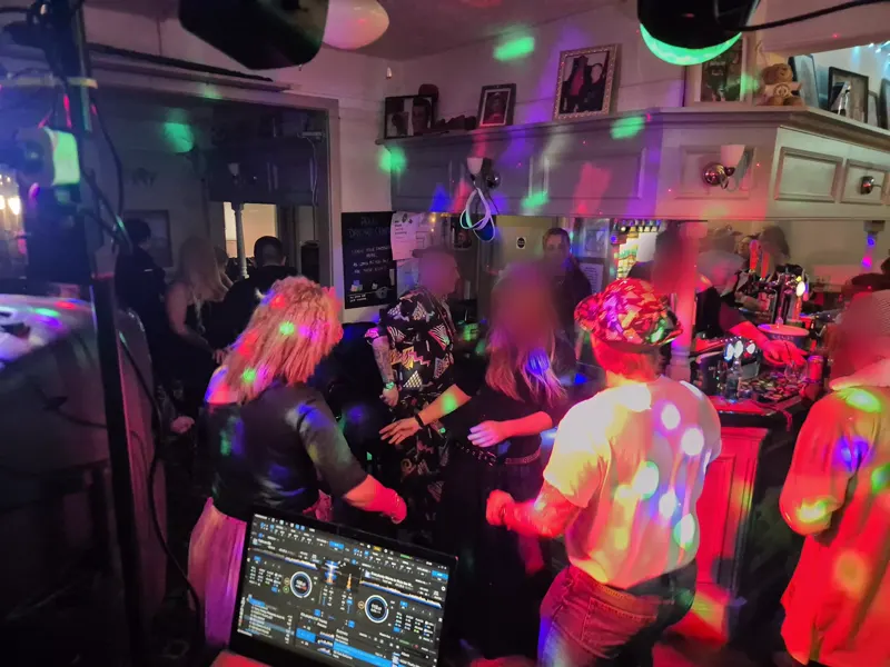 Guests in 80s outfits dancing in the bar under coloured lights